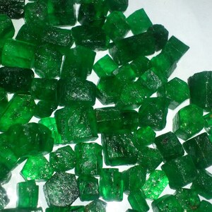 Peut inclure: Un grand tas d'émeraudes brutes non taillées. Les émeraudes sont d'une couleur vert foncé et présentent une variété de formes et de tailles.