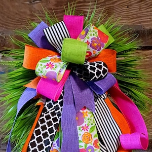 May include: A colorful bow made with various patterned ribbons, including floral, striped, and geometric designs. The bow is tied with a bright pink ribbon and features a lime green ribbon in the center.