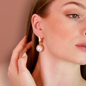 Könnte beinhalten: Goldene Creolen mit einem großen, weißen Perlenanhänger.