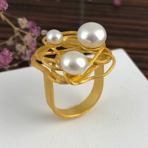 May include: A gold ring with a delicate, interwoven design, featuring four white pearls of varying sizes.