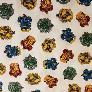 May include: White fabric with a repeating pattern of the Hogwarts house crests. The crests are in their traditional colors: Gryffindor (red and gold), Hufflepuff (yellow and black), Ravenclaw (blue and bronze), and Slytherin (green and silver).
