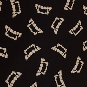 May include: Black fabric with a white repeated pattern of stylized vampire fangs.