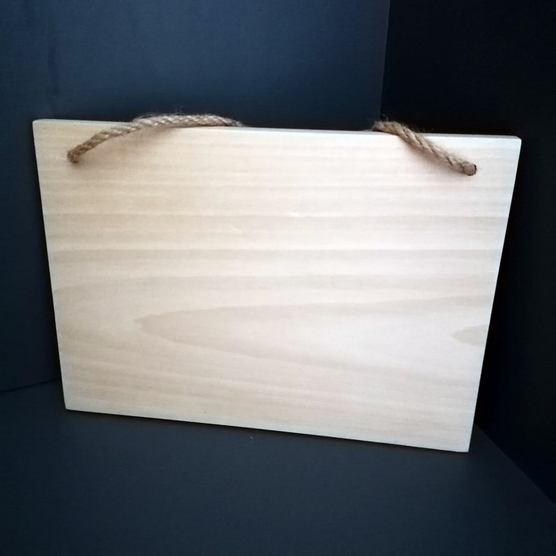 May include: A plain, light wood sign with a natural grain pattern. The sign has two holes at the top and is strung with a natural twine rope.