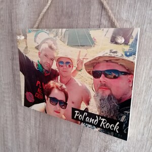 May include: A wooden sign with a photo of four people at a music festival. The sign has the text "Pol'and' Rock" printed on it.