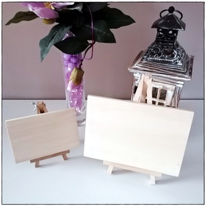 May include: Two blank wooden signs with easel stands. The signs are made of light wood and are both rectangular in shape. The signs are sitting on a white surface.