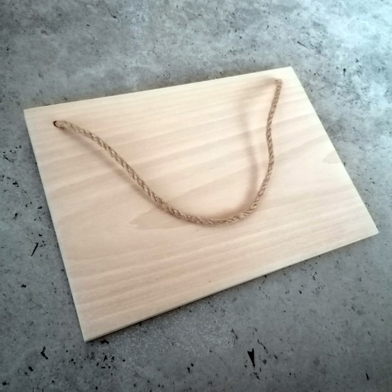 May include: A light wood rectangular sign with a natural finish. The sign has a jute rope hanger attached to the top.