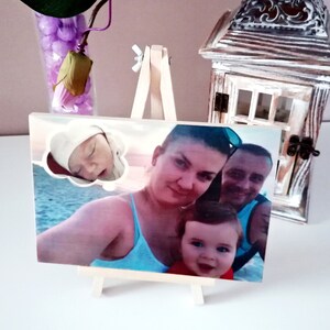 May include: A wooden easel with a photo of a family. The photo shows a woman, a man, and a young child. The woman is holding the child. The photo is on a white background. There is a small cloud with a baby sleeping inside the photo.