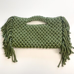 Könnte beinhalten: Eine grüne gehäkelte Tasche mit Fransen. Die Tasche hat einen einzigen Henkel und ist aus dickem, strukturiertem Garn gefertigt.