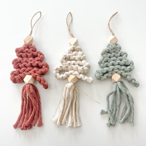 May include: Three handmade Christmas tree ornaments. The ornaments are made of yarn and have a wooden bead at the top. The trees are red, white with gold glitter, and green.