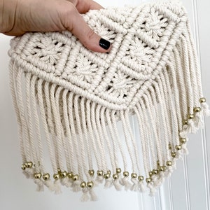 May include: A white crocheted bag with a fringe and gold beads. The bag is made with a diamond pattern.