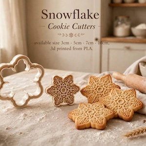 May include: A set of snowflake cookie cutters and matching embossed cookies. The text reads: Snowflake Cookie Cutters, available size 3cm - 5cm - 7cm - 10cm, 3d printed from PLA. The cutters are light-coloured and the cookies feature intricate patterns.