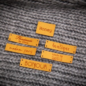 May include: Five yellow leather labels with brown text. The labels read "Honey", "Handmade by Olivia", "madam paris", "boutique", and "Made by ISABELLA".