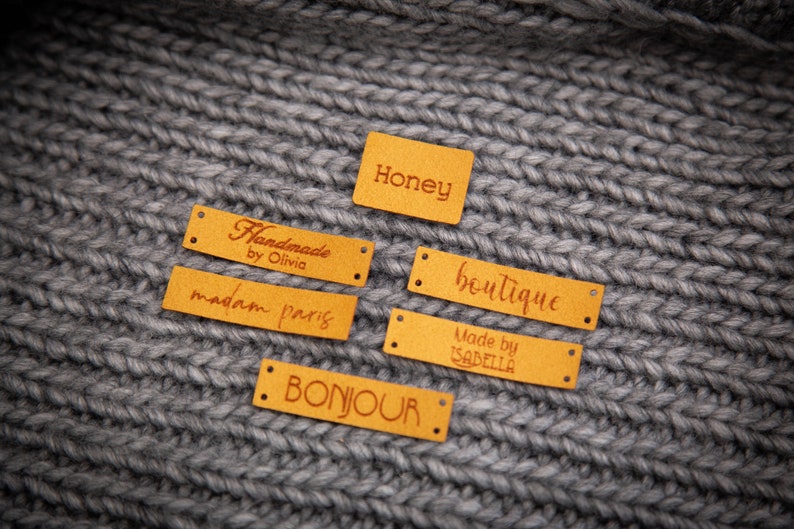 May include: Five yellow leather labels with brown text. The labels read "Honey", "Handmade by Olivia", "madam paris", "boutique", and "Made by ISABELLA".