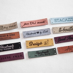 May include: A collection of 11 different leather labels with various text and designs. The labels are in different colors, including brown, beige, gray, blue, green, and red. The text on the labels includes "Thread & Vine Collective", "Handmade by Monsini G", "Sraigė", "Sweet Amelia's", "Village Swag", "Handmade by Cathy Barry", "O by Hala", "foor DIJ maakt", "STACAZZI", "U-boulte", and "Art on Col".
