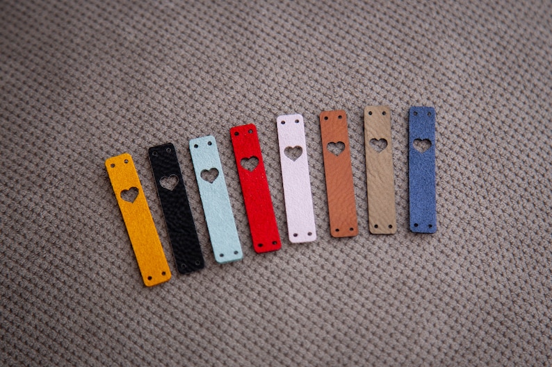 May include: Ten leather straps with a heart-shaped cutout in various colours, including yellow, black, light blue, red, white, brown, beige, and blue.