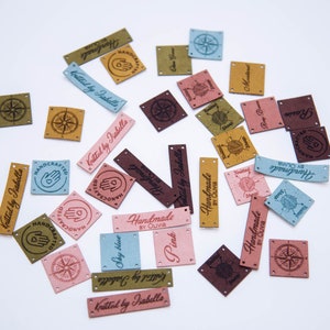 May include: Assortment of colorful leather labels with various designs and text, including "Handmade by Olivia", "Knitted by Isabelle", and "Handcrafted".
