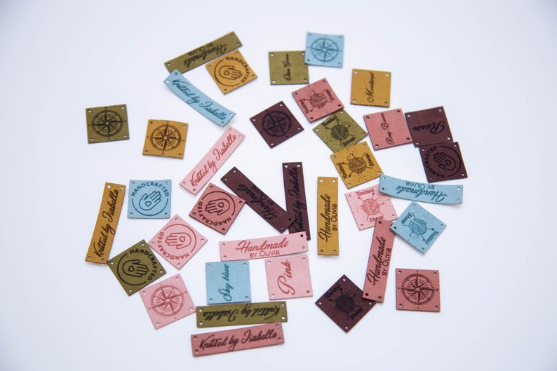May include: Assortment of colorful leather labels with various designs and text, including "Handmade by Olivia", "Knitted by Isabelle", and "Handcrafted".