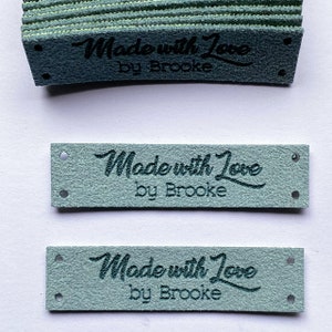 May include: A stack of light blue fabric labels with the text "Made with Love by Brooke" in black lettering.