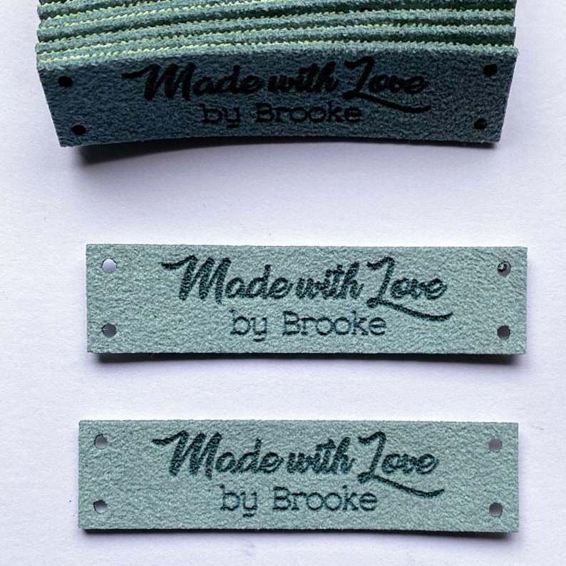 May include: A stack of light blue fabric labels with the text "Made with Love by Brooke" in black lettering.