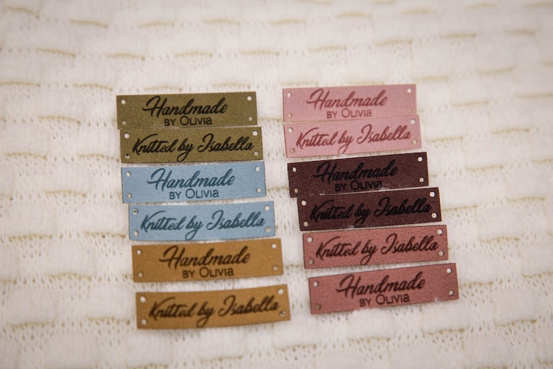 May include: A set of eight brown, pink, and blue leather labels with the text "Handmade by Olivia" and "Knitted by Isabella" in a cursive font.