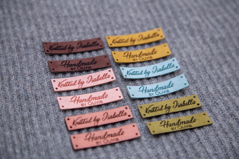 May include: Ten fabric labels with different colors and text. The labels say "Knitted by Isabella" and "Handmade by Olivia".