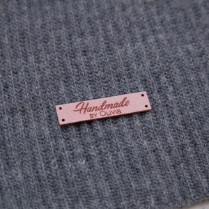 May include: A brown leather label with the text "Handmade by Olivia" in pink lettering.
