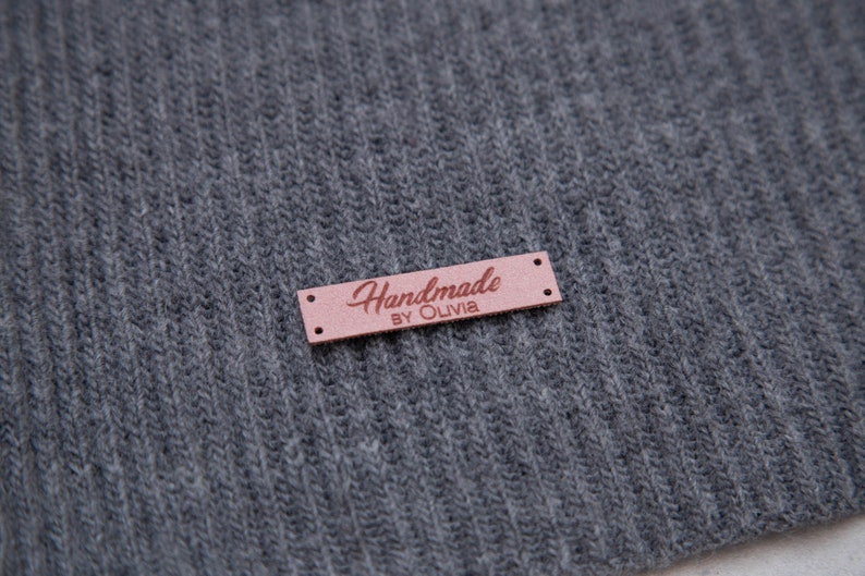 May include: A brown leather label with the text "Handmade by Olivia" in pink lettering.