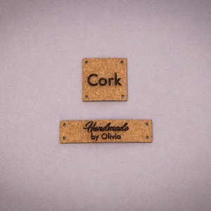 Può includere: Due etichette in sughero marrone con testo nero. L'etichetta superiore dice "Cork" e l'etichetta inferiore dice "Handmade by Olivia".