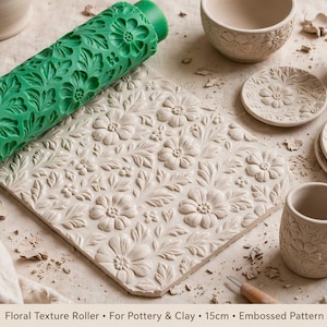 May include: A green cylindrical texture roller with an embossed floral pattern, alongside a flat square slab of clay featuring the same imprinted floral design. Several ceramic pieces, including a bowl, small plates, and a mug, display the pattern.