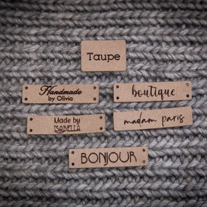 May include: Five brown leather labels with different text on each. The labels read "Taupe", "Handmade by Olivia", "boutique", "Made by ISABELLA", and "BONJOUR".