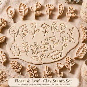 Può includere: Un set di 14 timbri per argilla color beige con vari disegni di fiori e foglie, disposti attorno a un pezzo di argilla appiattito impresso con gli stessi motivi. Include due tazze in ceramica con motivi botanici in rilievo e un utensile.