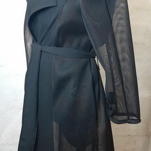 May include: A black trench coat with a mesh overlay. The coat has a belt and a button closure.
