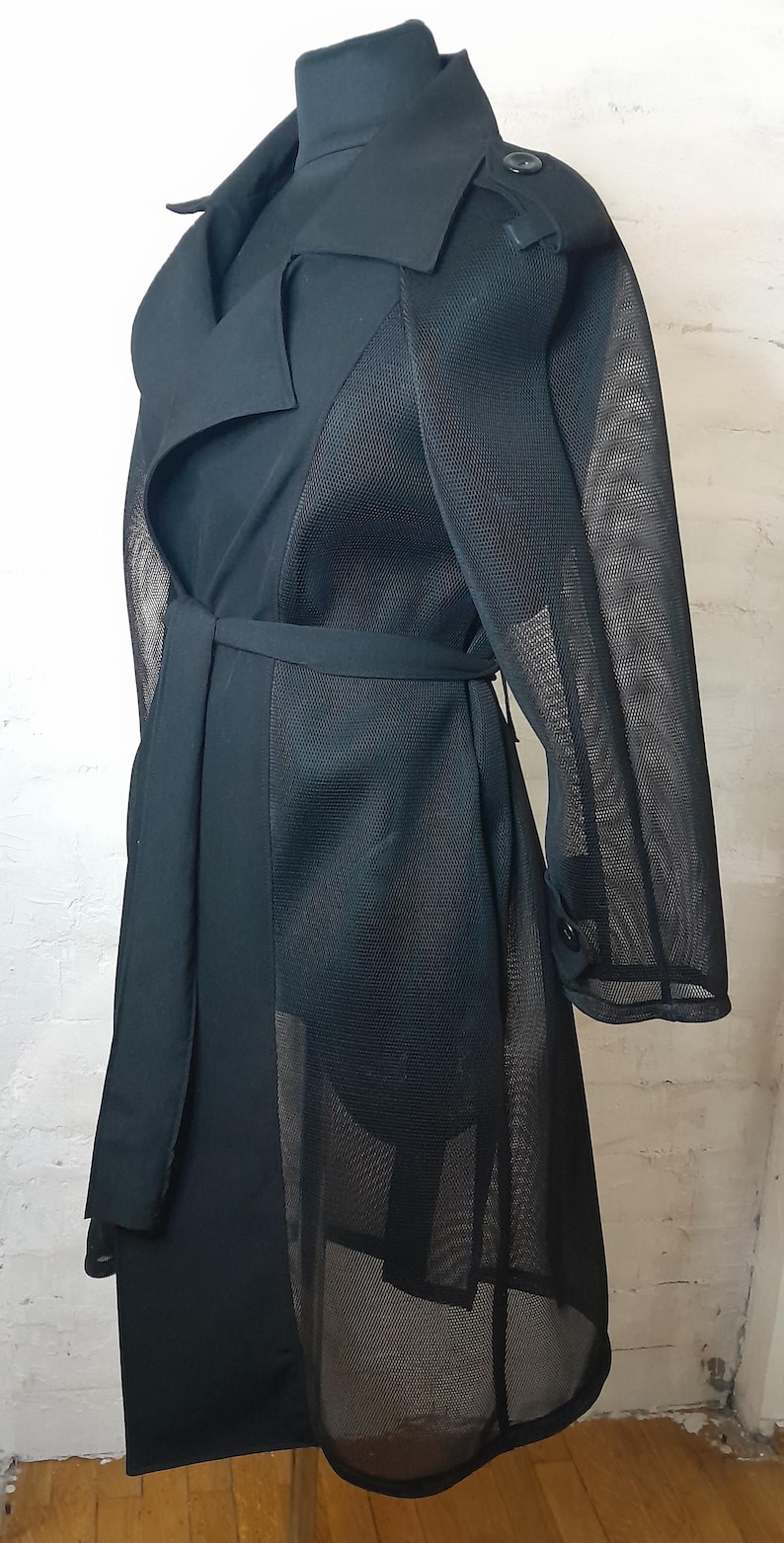 May include: A black trench coat with a mesh overlay. The coat has a belt and a button closure.