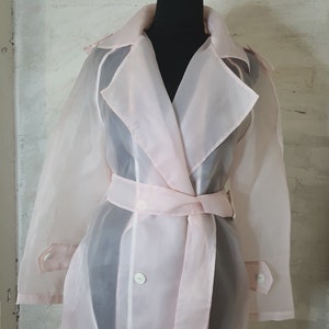 May include: A sheer pink trench coat with a belt and buttons. The coat is made of a lightweight, translucent fabric.