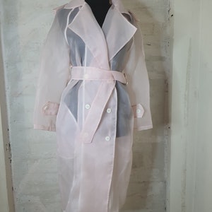 May include: A sheer pink trench coat with a double breasted closure and a belt. The coat is made of a lightweight, translucent fabric.
