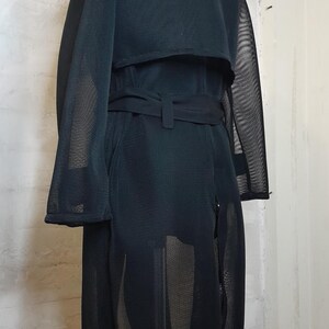 May include: A black mesh trench coat with a belt. The coat is see-through and has a long, flowing silhouette.