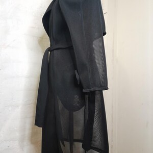 May include: Black mesh long-sleeved coat with a wrap-style collar and a belt. The coat has a sheer, see-through design.