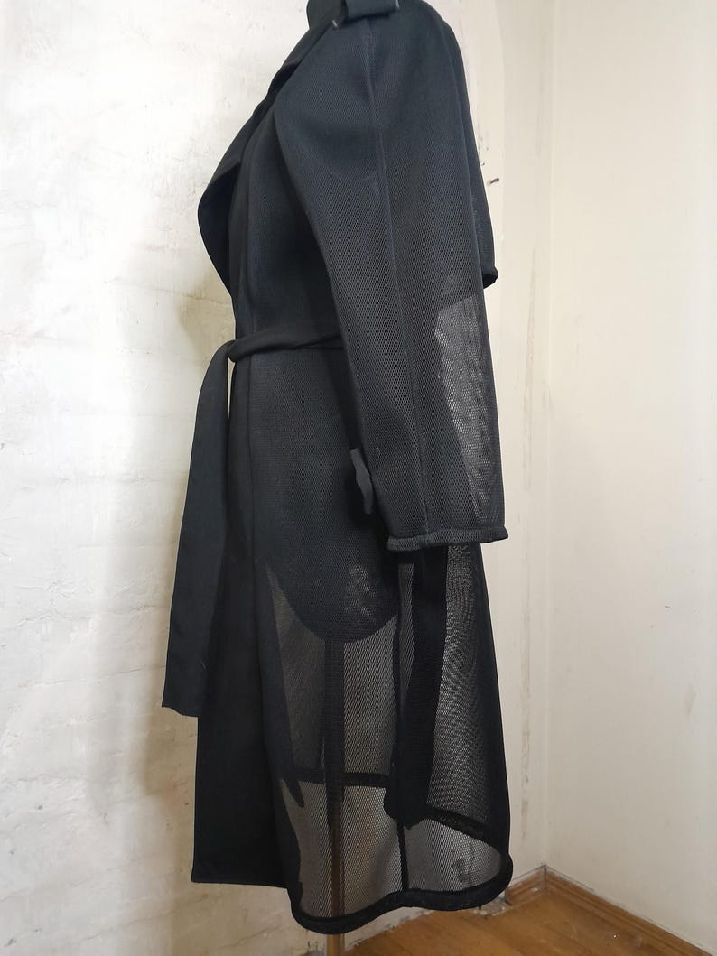 May include: Black mesh long-sleeved coat with a wrap-style collar and a belt. The coat has a sheer, see-through design.