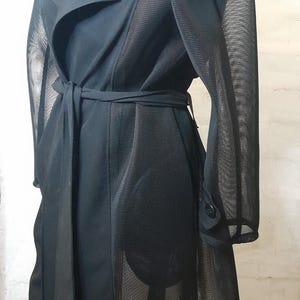 May include: A black trench coat with a mesh panel on the back and sleeves. The coat has a belt and a button closure.