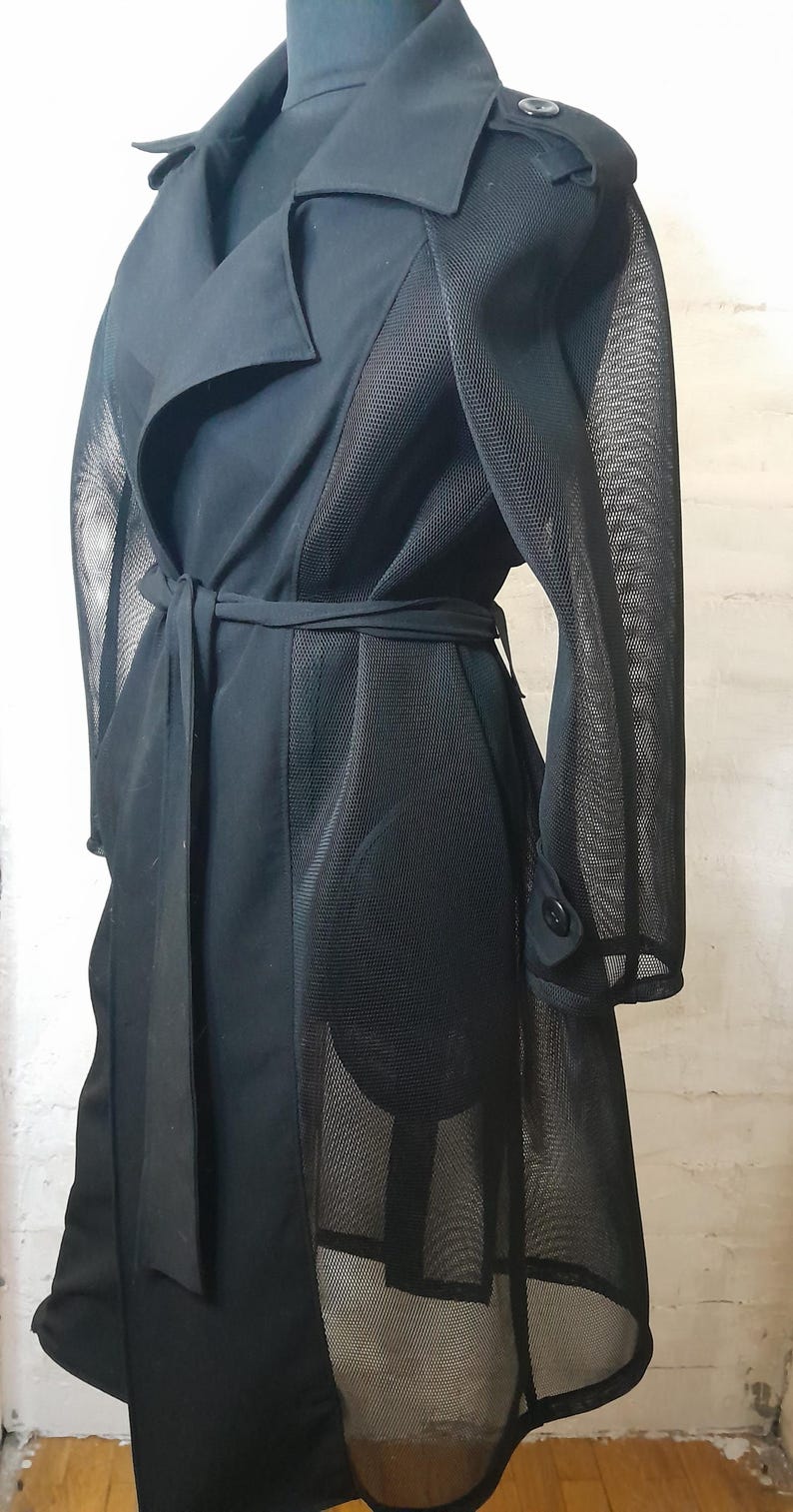May include: A black trench coat with a mesh panel on the back and sleeves. The coat has a belt and a button closure.