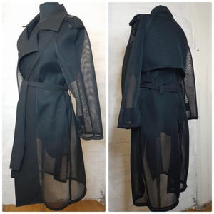 May include: A black mesh trench coat with a long, flowing silhouette. The coat has a classic trench coat design with a collar, belt, and pockets. The mesh fabric gives the coat a sheer and airy look.