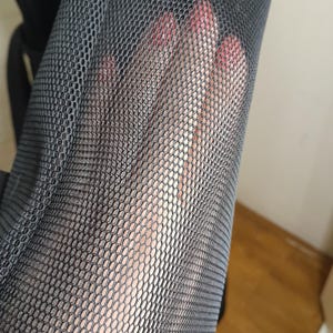 May include: Close-up of black mesh fabric with a fine, even weave. The fabric is soft and flexible, and it has a slightly textured surface.