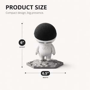 May include: A white astronaut-shaped speaker with a black speaker dome. The figure is standing on a gray, textured base. The text "USA" is on the chest. The product size is 15.2 cm in height and 16.5 cm in width.