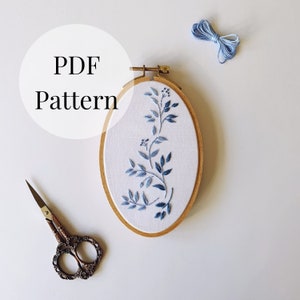 May include: A white embroidery hoop with a blue floral design, a pair of small scissors, and a skein of blue embroidery floss. The hoop has the text "PDF Pattern" written on it.