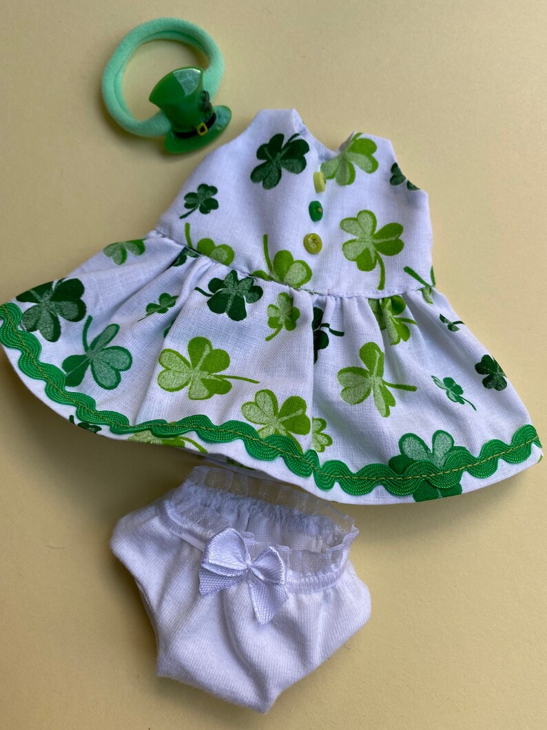 May include: A white dress with a green shamrock print, a white diaper with a white bow, and a green shamrock hair clip.