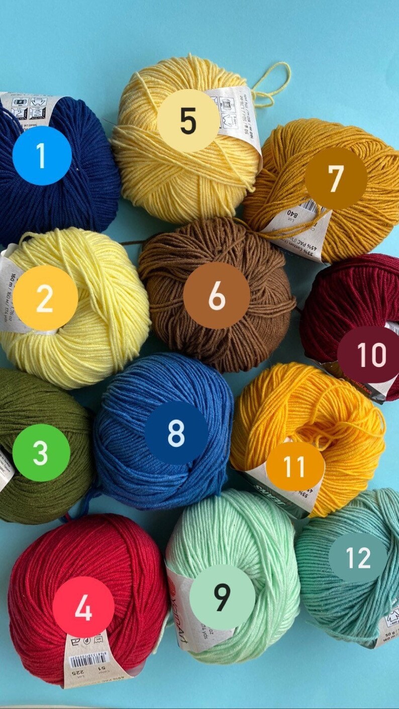 May include: Twelve balls of yarn in various colors, including yellow, blue, green, red, brown, and orange. The balls are numbered 1 through 12.