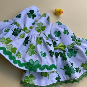 May include: A white dress with a green shamrock print and green trim. The dress has a ruffled skirt and a lace trim.