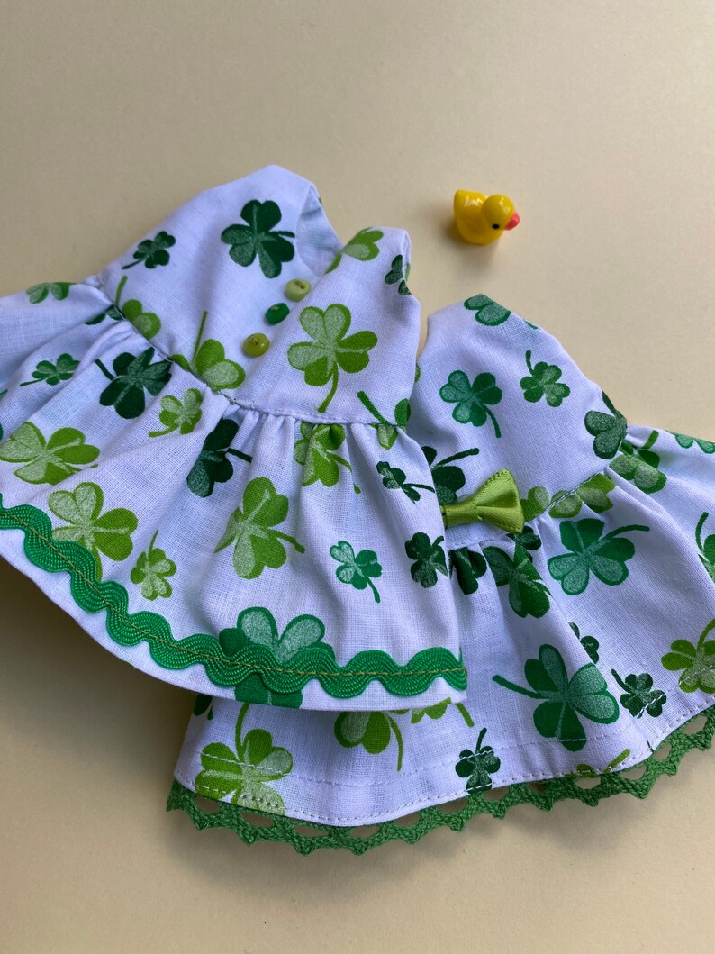 May include: A white dress with a green shamrock print and green trim. The dress has a ruffled skirt and a lace trim.