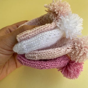 May include: Three knitted hats with pom-poms in shades of pink and white.