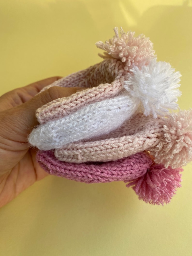 May include: Three knitted hats with pom-poms in shades of pink and white.